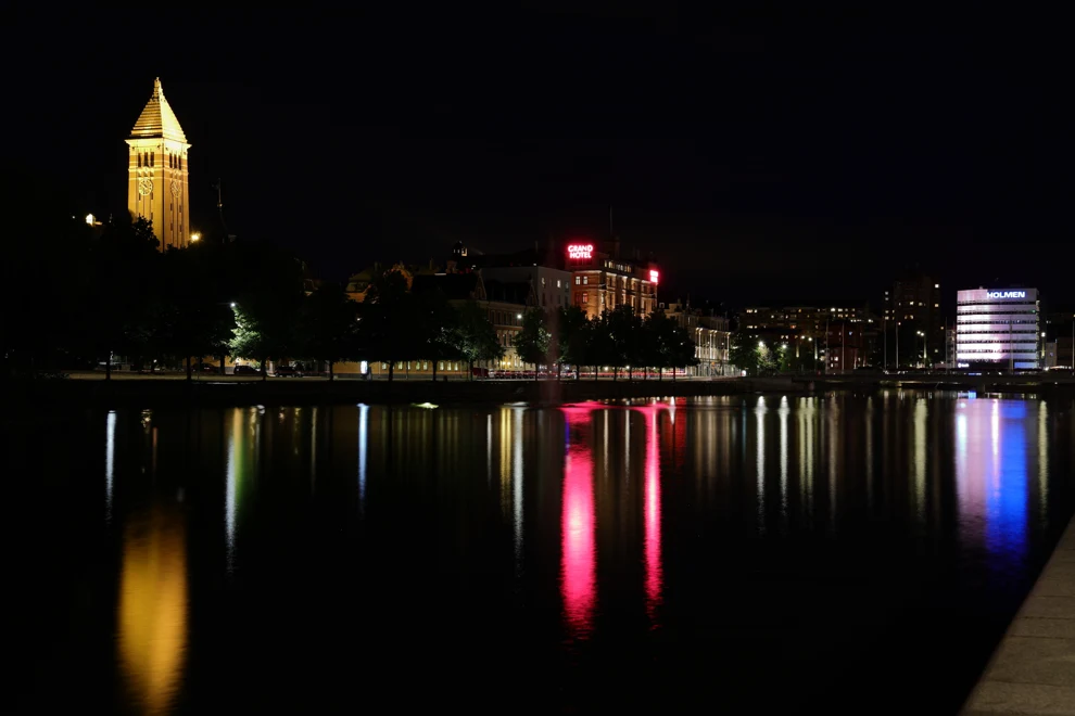 Norrköpings stadskärna reflekteras mot vatten i blåa, gula och röda färger.